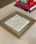 Framed 3D city map wall art with white buildings, displayed on a modern coffee table