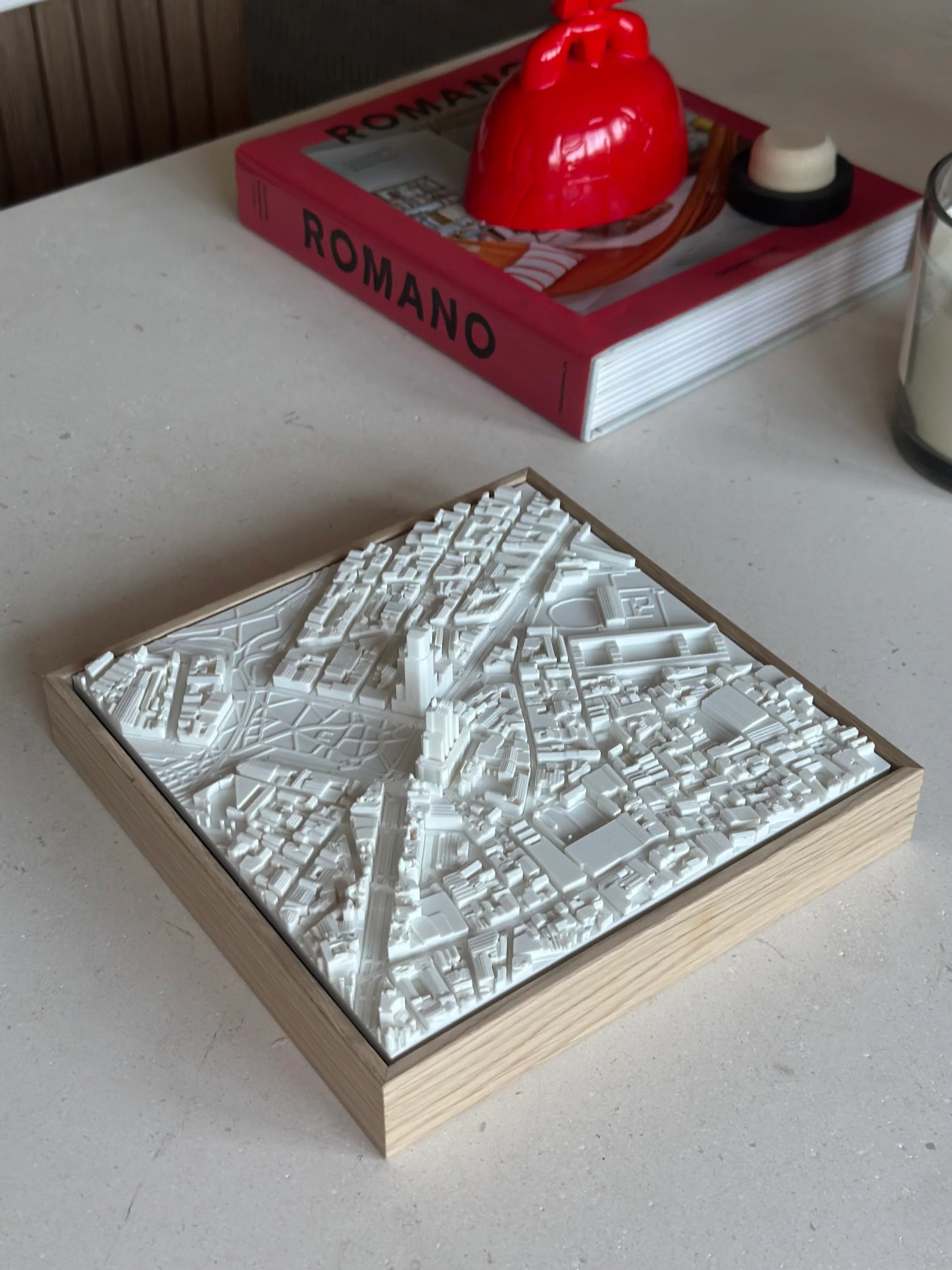 3D city map wall art in white on a wooden base, displayed on a minimal tabletop.