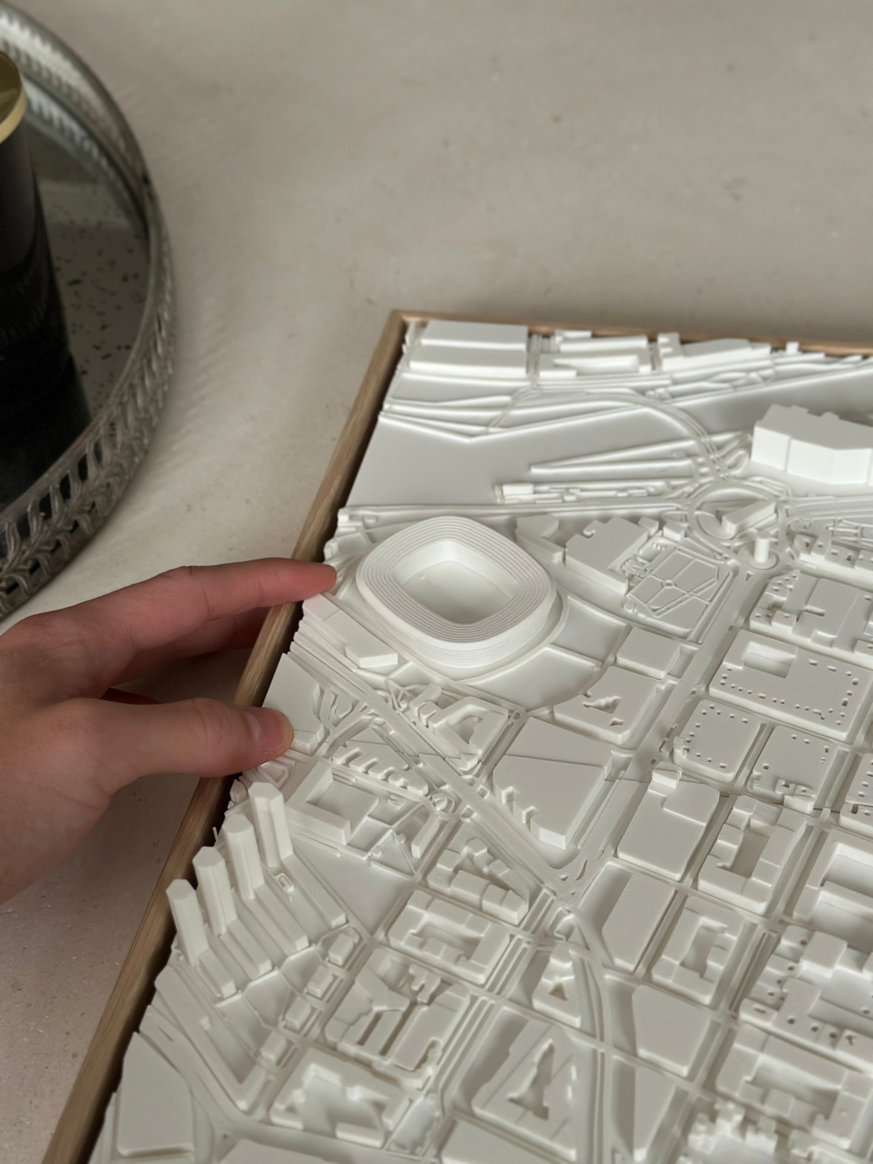 Hand touching 3D city map wall art showcasing detailed urban buildings and street layout