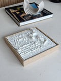 Framed 3D city map art in white on a light wood frame, displayed on a modern table