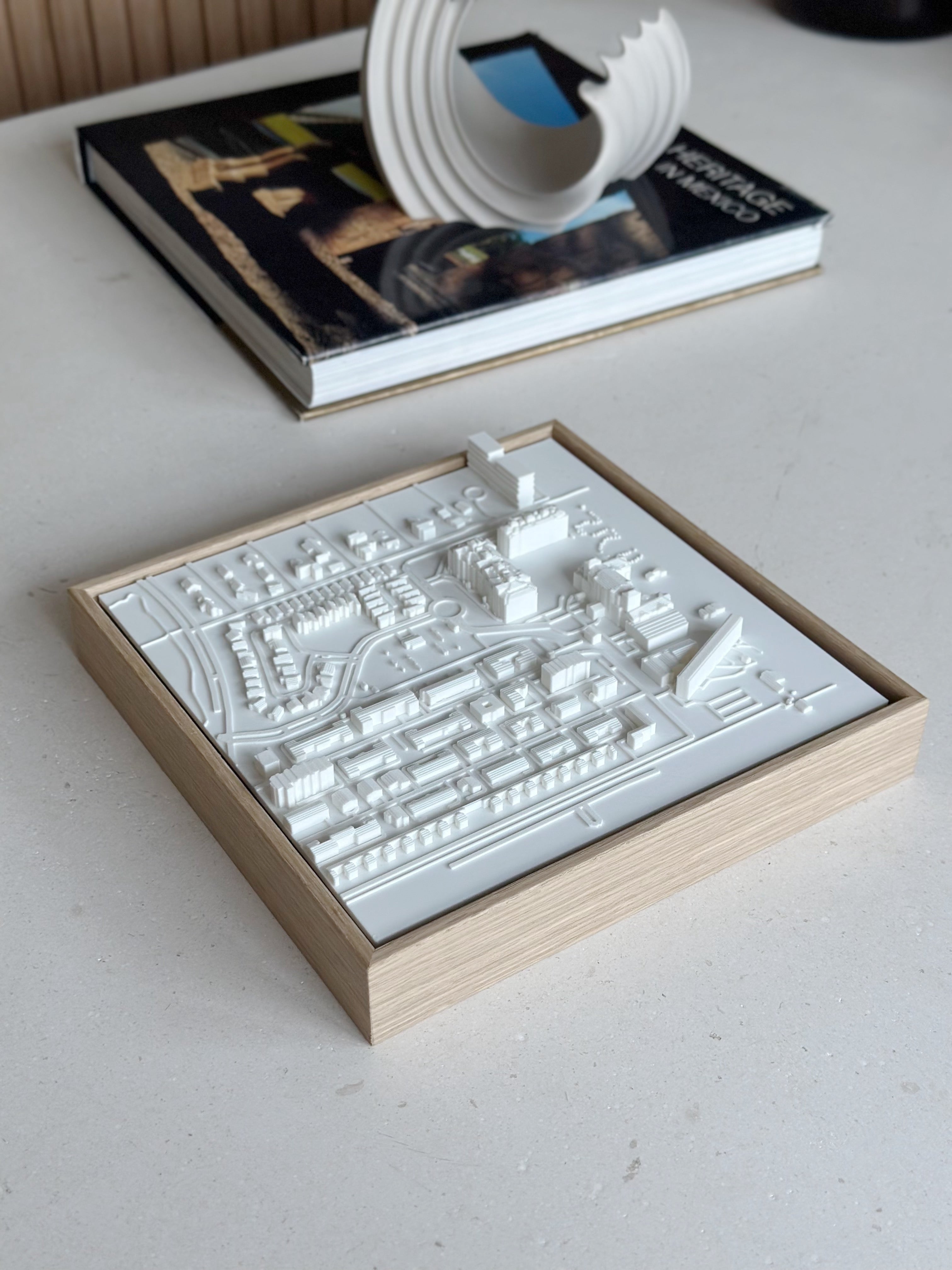 Framed 3D city map art in white on a light wood frame, displayed on a modern table