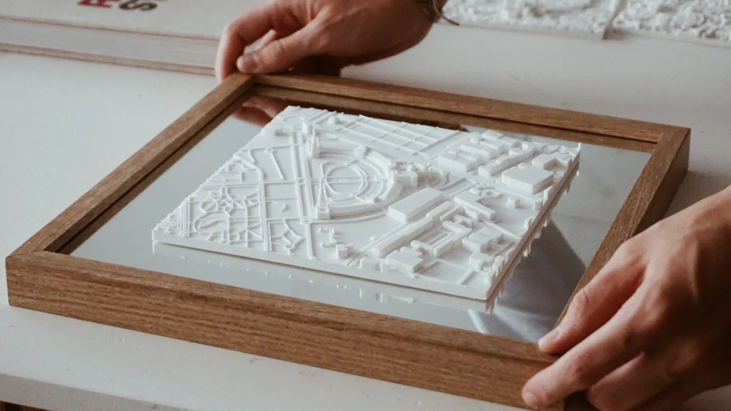 Hands holding a wooden frame with a white 3D city map wall art, home decor piece.