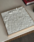 3D city map wall art in white, detailed urban streets and buildings, decorative frame on table