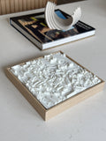 3D city map wall art in a wooden frame on a modern coffee table, with decor and a book.
