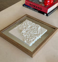 Framed 3D city map decor piece with white buildings on a table, modern home setting