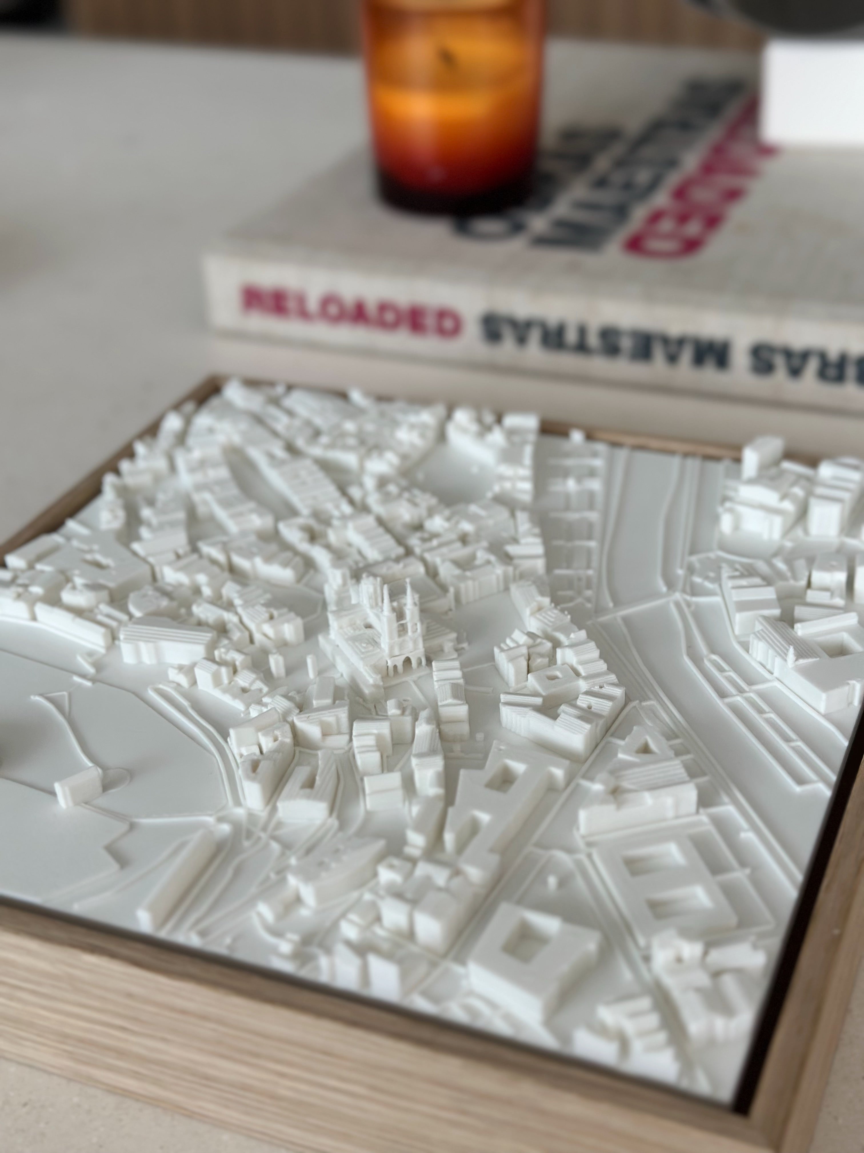 3D city map wall art in a wooden frame on a table, with candle and book in background