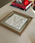 Framed 3D city map decor in white on a table, with books and modern home accents