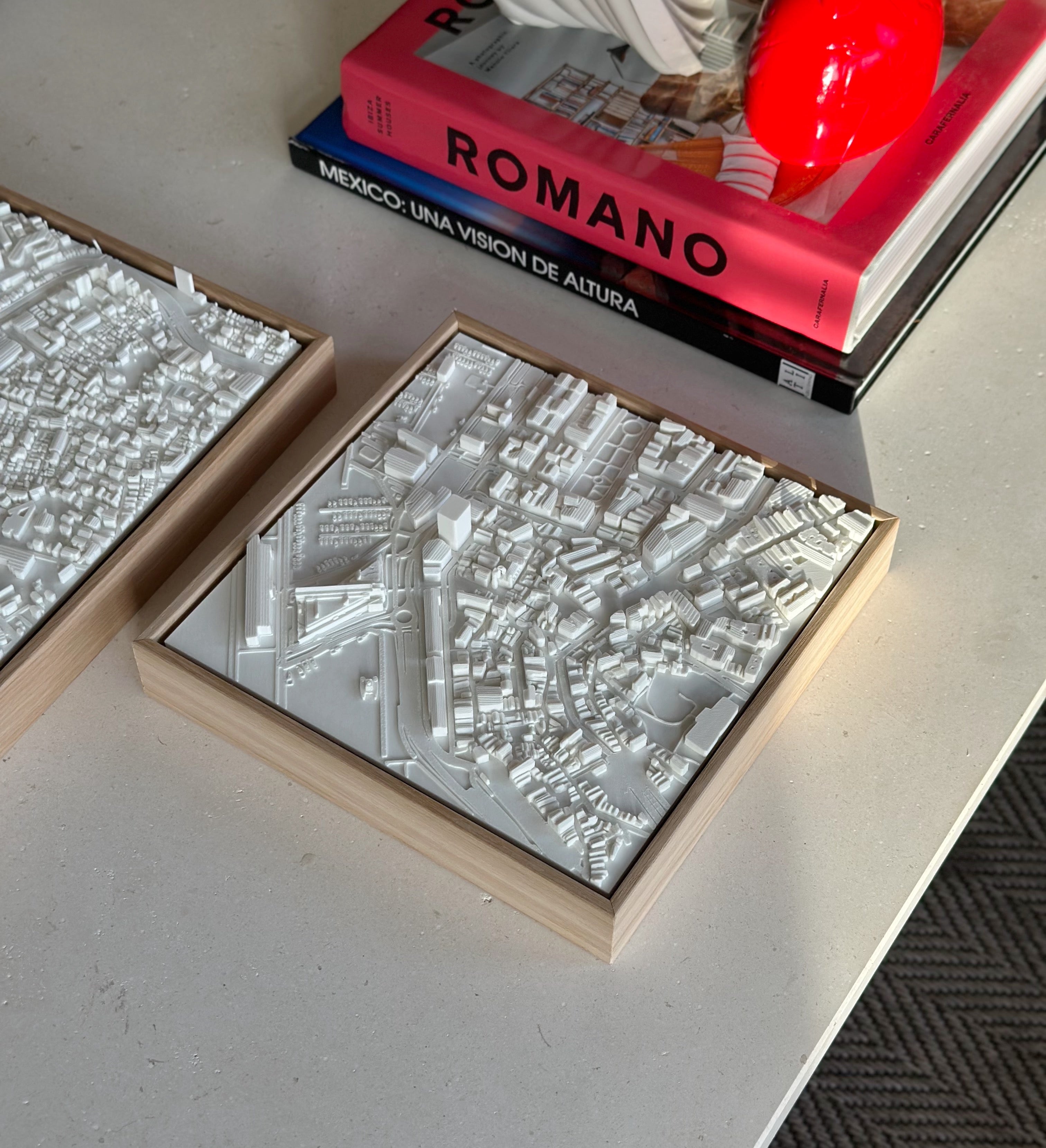 White 3D city map wall art in wooden frame on table beside design books