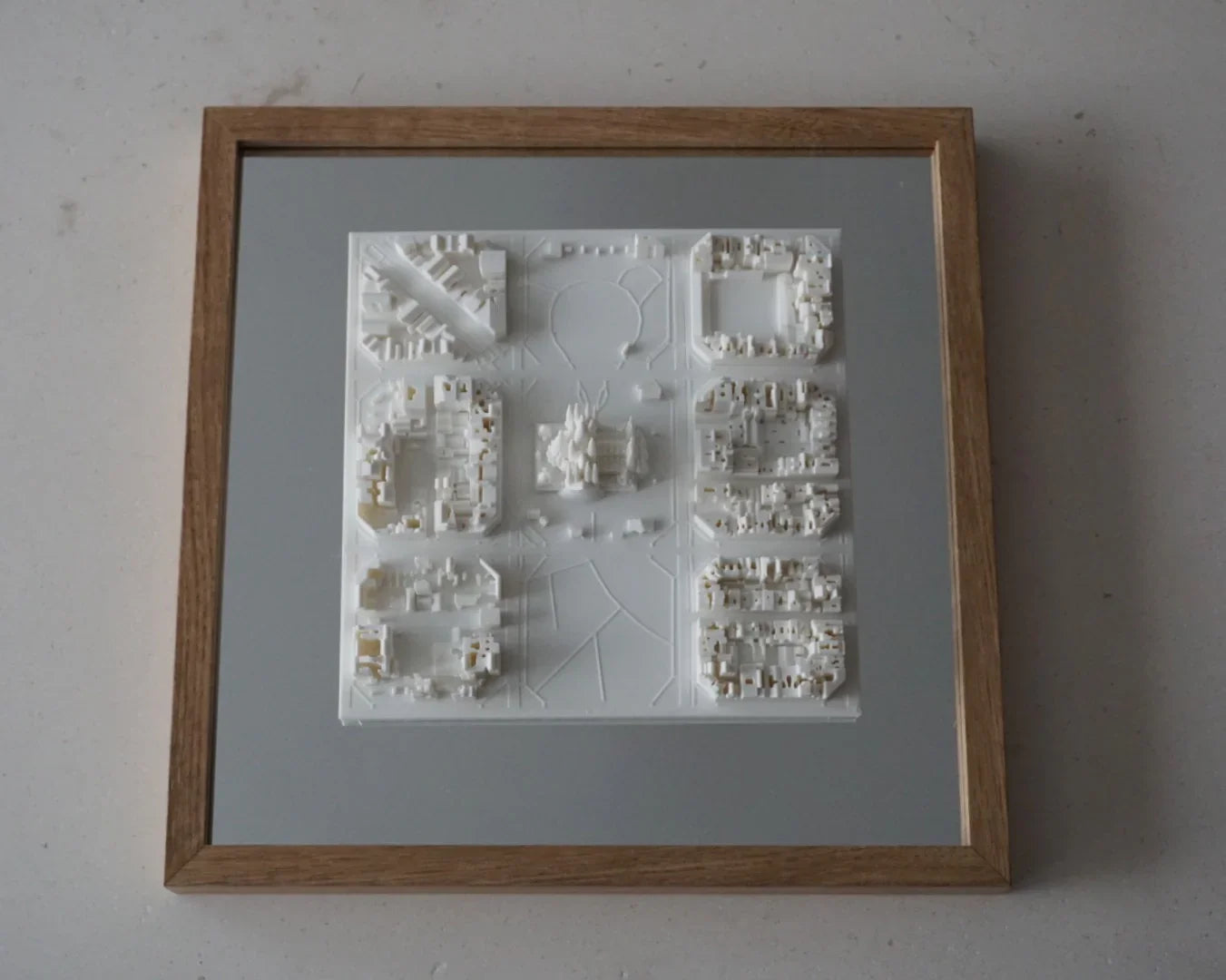 Framed 3D city map wall art with white architectural buildings on a gray background.