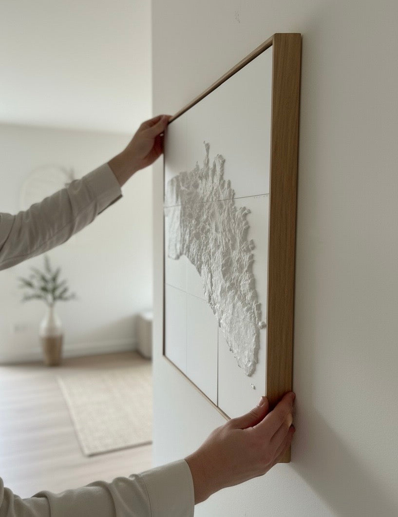 Person hanging a framed 3D city map wall art in a modern living room
