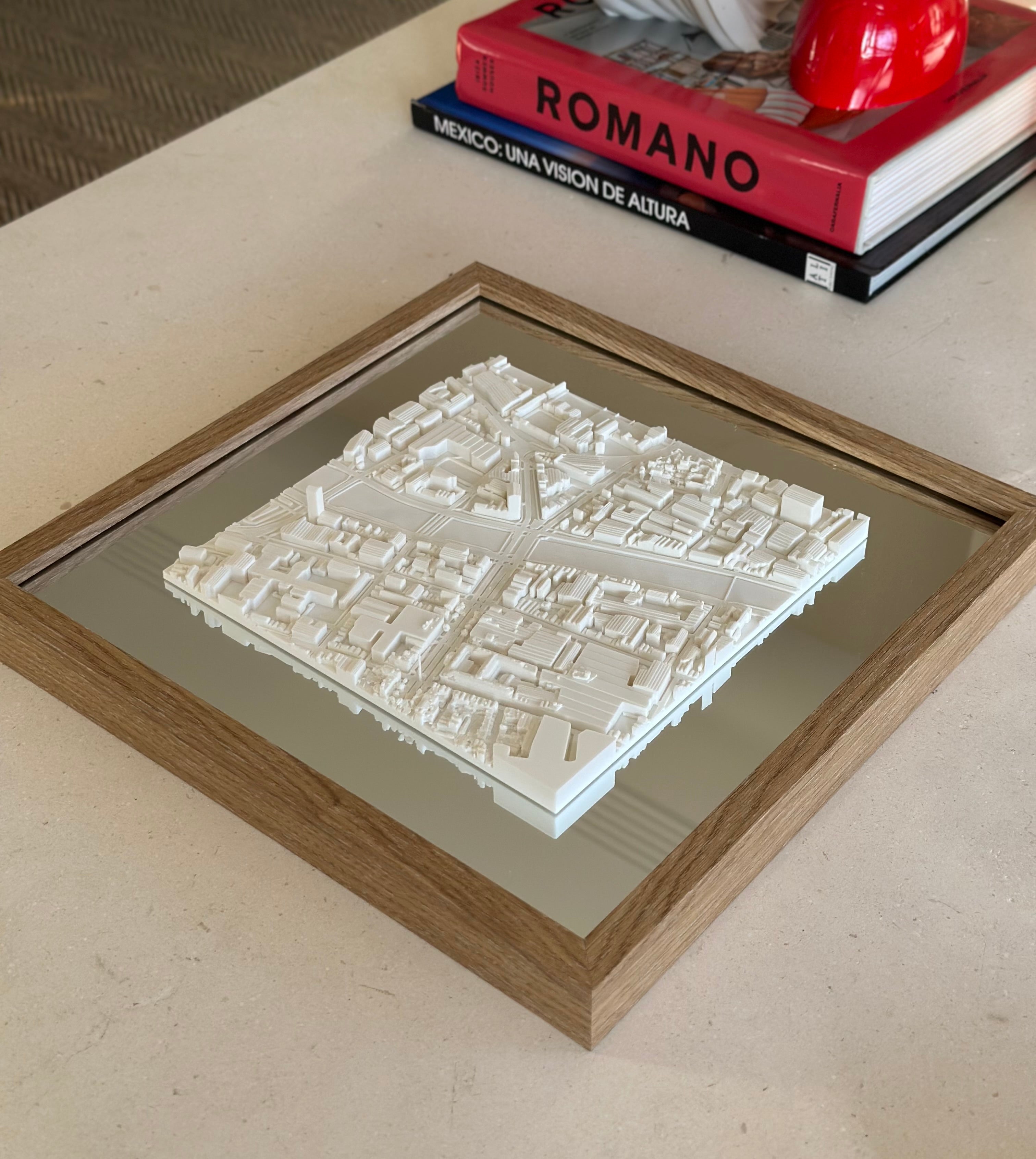 3D city map wall art in a wooden frame on a table beside design books