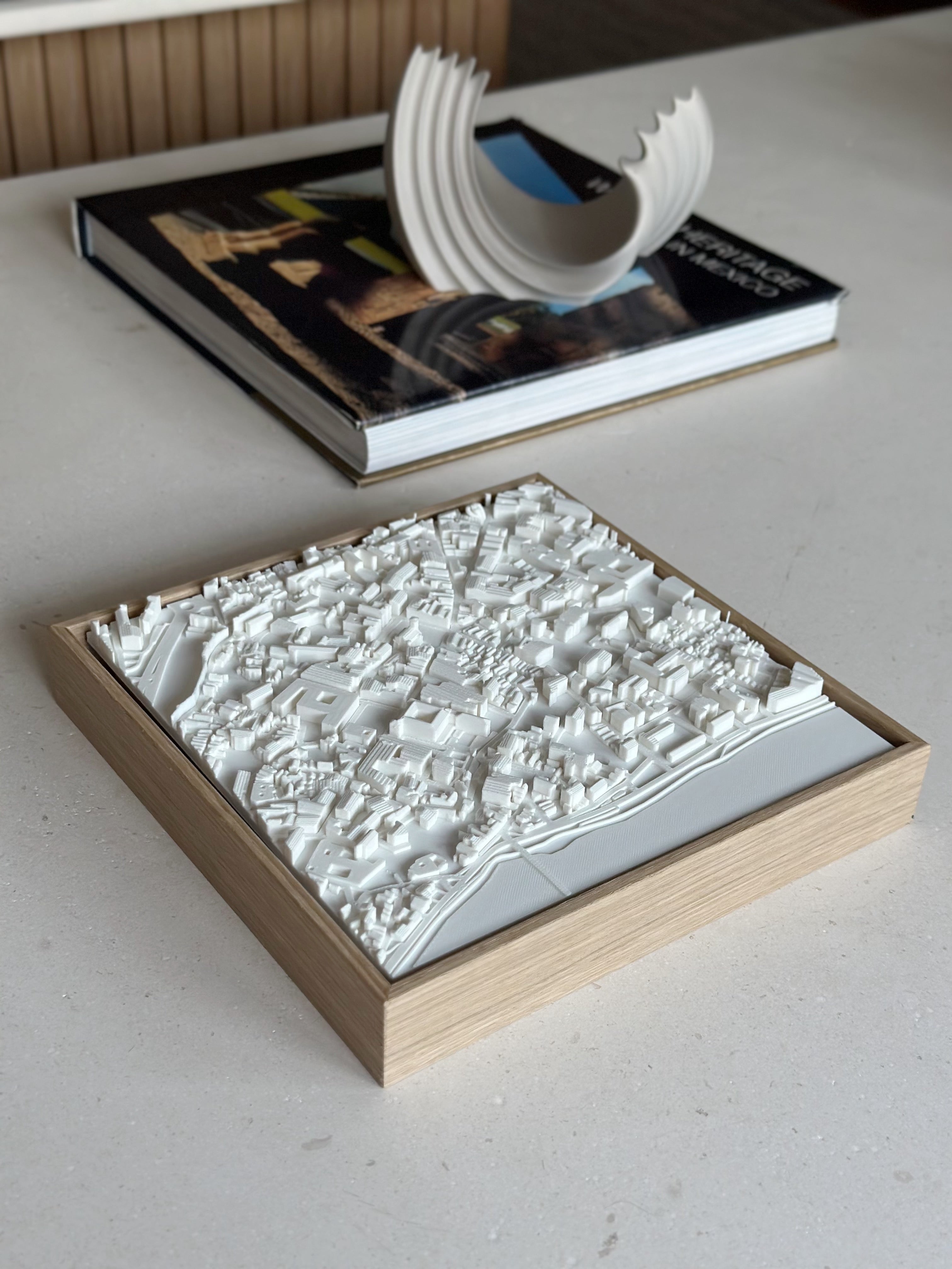 3D city map art in wooden frame on a modern coffee table, decorative book in background