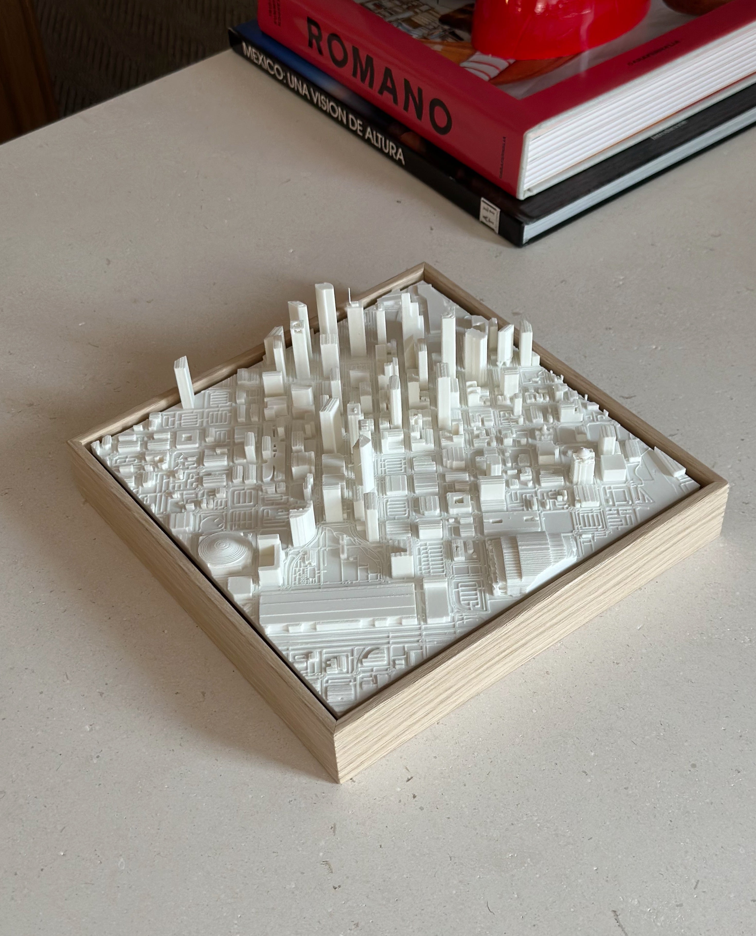 3D city map wall art in white frame on beige table, with books in the background
