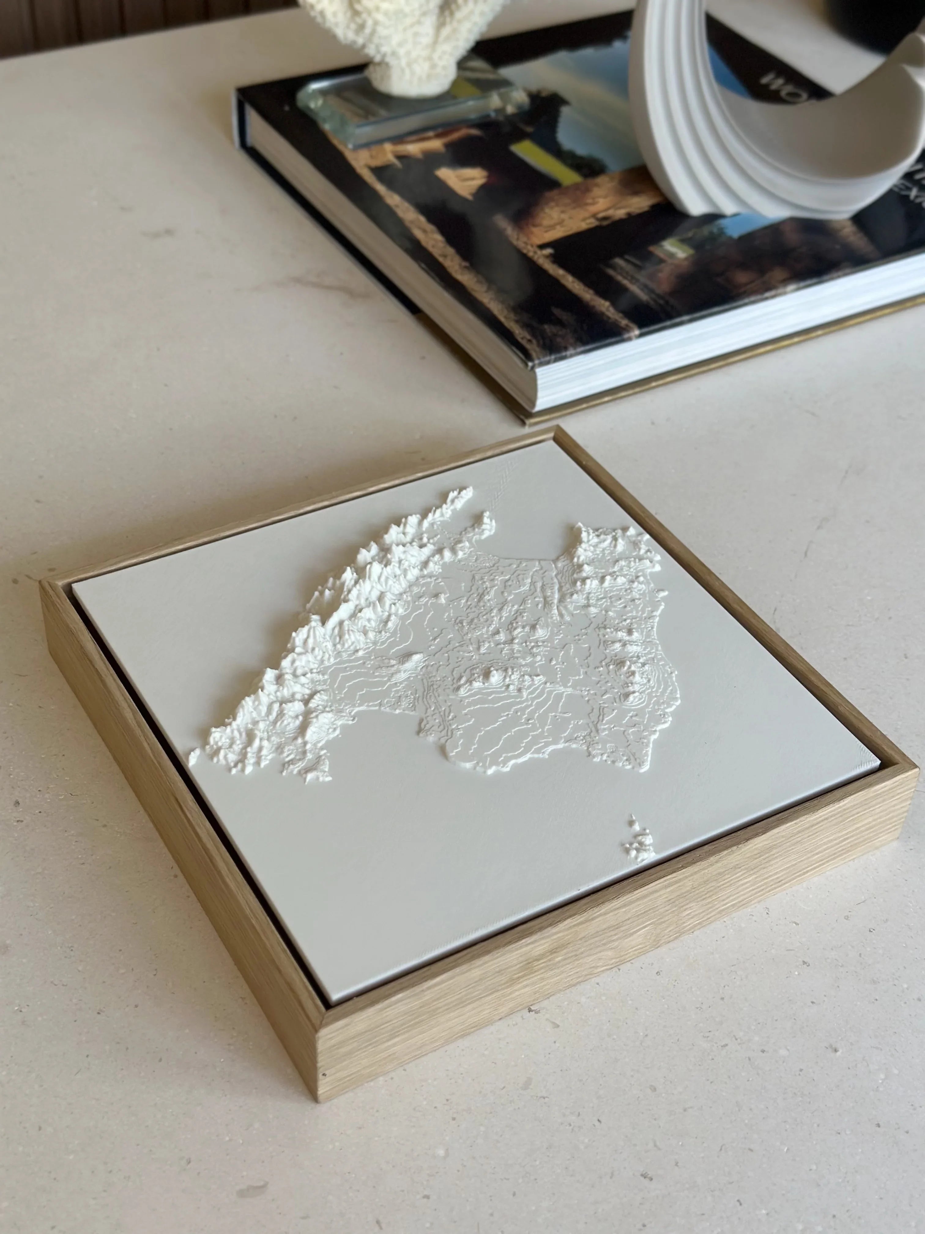 3D city map wall art in a wooden frame on a modern table with decor and a book