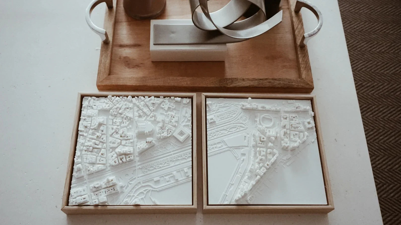 Two 3D city map wall art pieces in white frames on a table next to decorative objects